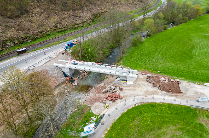 Luftaufnahme einer neuen Autobahnbrücke und Straße im Bau in einer hügeligen Landschaft.