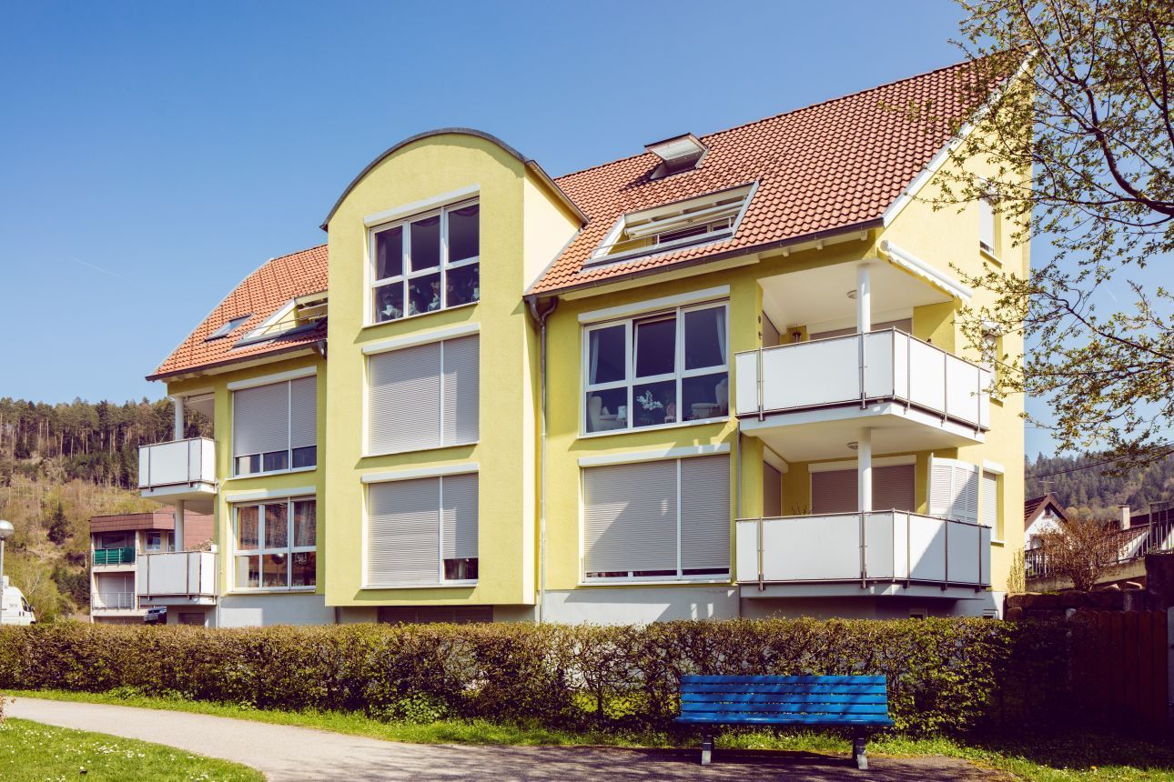 Gelbes Mehrfamilienhaus mit Balkonen und Garten.